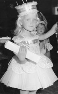 Black and white image of the author as a little girl, dressed in fancy dress as a birthday cake.